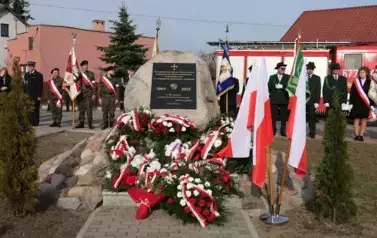 Pomnik udekorowany kwiatami i flagami. Za pomnikiem poczty sztandarowe.