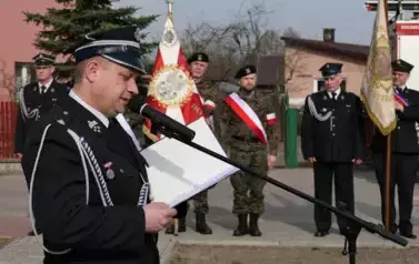 Komendant Ochotniczych Straży Pożarnych przemawia. W tle poczty sztandarowe.