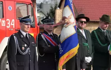 Poczet sztandarowy OSP w Pogorzelcu na tle dużego samochodu strażackiego.
