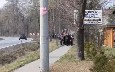 Przemarsz uczestnik&oacute;w uroczystości pod pomnik w Gwizdałach. po lewej stronie jadący samoch&oacute;d.