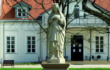 rzeżba Matki Boskiej na tle pałacu w Łochowie
