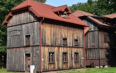 Drewniany budynek na tle zielonych drzew. Jest to wyłuszczarnia nasion.