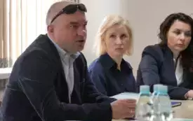 Troje uczestnik&oacute;w spotkania siedzi przy stole konferencyjnym. 